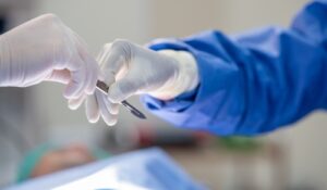 Close-up view of a surgeon's gloved hands passing a surgical instrument to another medical professional during an operation, emphasizing precision and teamwork in a sterile environment.