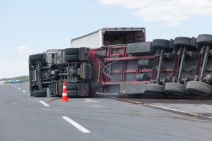 An overturned truck spilling its cargo on an interurban road, with debris scattered around and emergency responders on the scene