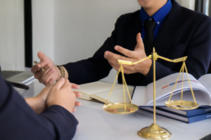 Two people in suits discussing something across a table with a golden scale of justice in the foreground