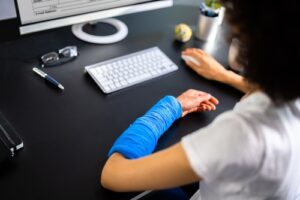 Person with a blue cast on their arm working at a computer desk