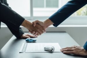 Two people shaking hands over a contract with car keys on the table