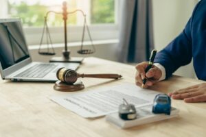 Lawyer signing a document with a gavel and scale of justice on the desk