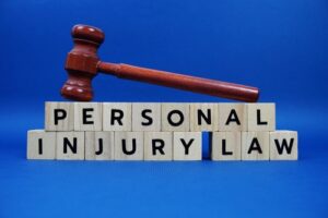 Wooden gavel resting on letter blocks that spell out 'PERSONAL INJURY LAW' against a blue background, symbolizing legal concepts and the judicial system related to personal injuries.