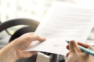 Close-up of a man's hand about to sign a legal document, indicating the process of leasing or purchasing a new or used car.