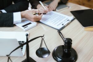 Close-up of a male lawyer in a suit reviewing contract documents with a wooden gavel placed on the table in a courtroom setting. The scene emphasizes justice and law, depicting the professional environment of legal work.