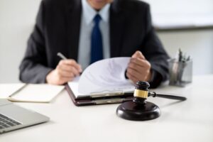 A lawyer drafts a legal document at a desk, surrounded by stationery and a laptop, in a casual law firm office atmosphere. 