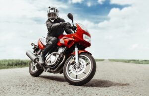 A man rides a motorcycle toward the camera on the highway. Another man on a red motorcycle turns in front of the camera.